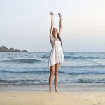 Mujer reduciendo el estrés en la playa vestida de blanco
